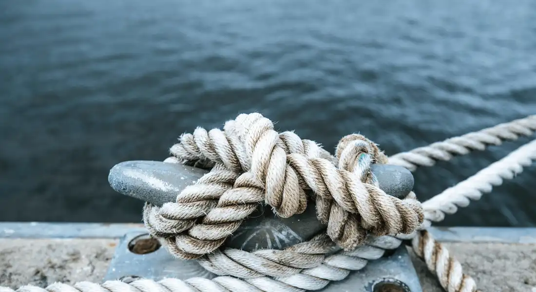 A rope tied to a dock with water in the background.