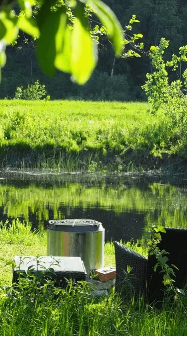 A riverside retreat with a cozy chair beside a crackling firepit on lush grass, offering a perfect spot to unwind and enjoy nature's serenit