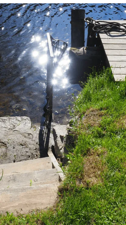 An idyllic riverside scene with a wooden jetty, where people enjoy bathing in the serene waters on a sunny day.